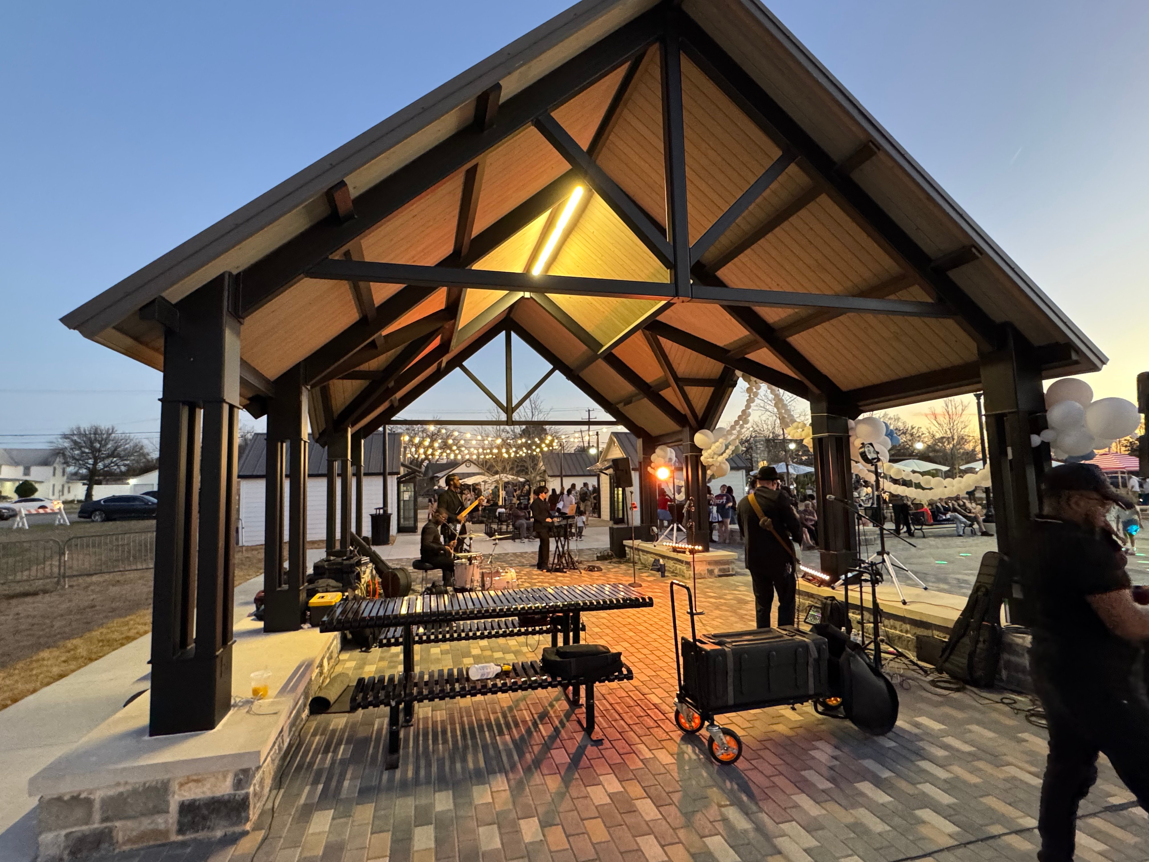 Evening view of the Geyer Commons pavilion in Mansfield, Texas, illuminated during a community event with live music, gathering spaces, and outdoor seating.