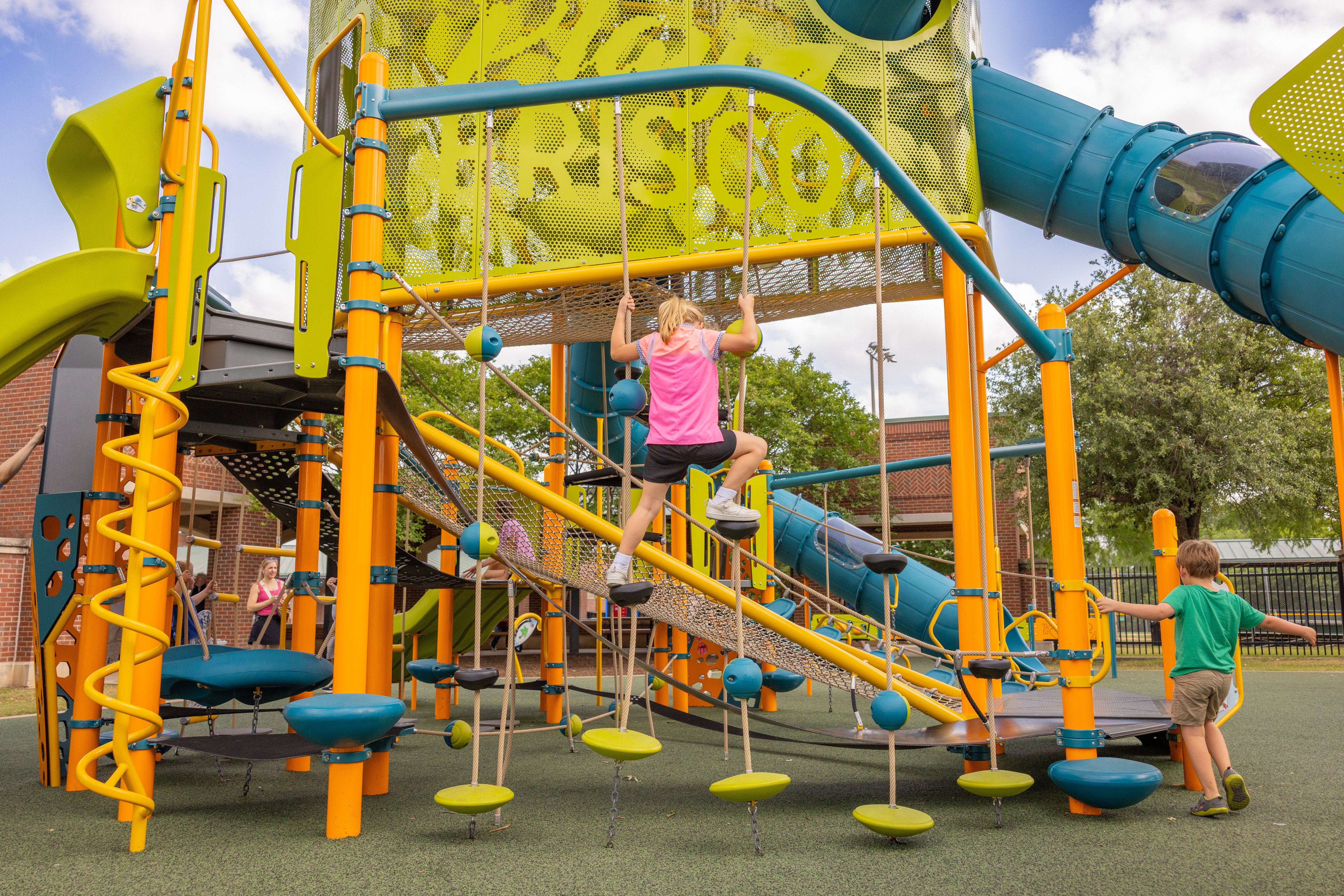 Children ages 5-12 climbing the Voloair Tower playground structure at Harold Bacchus Community Park