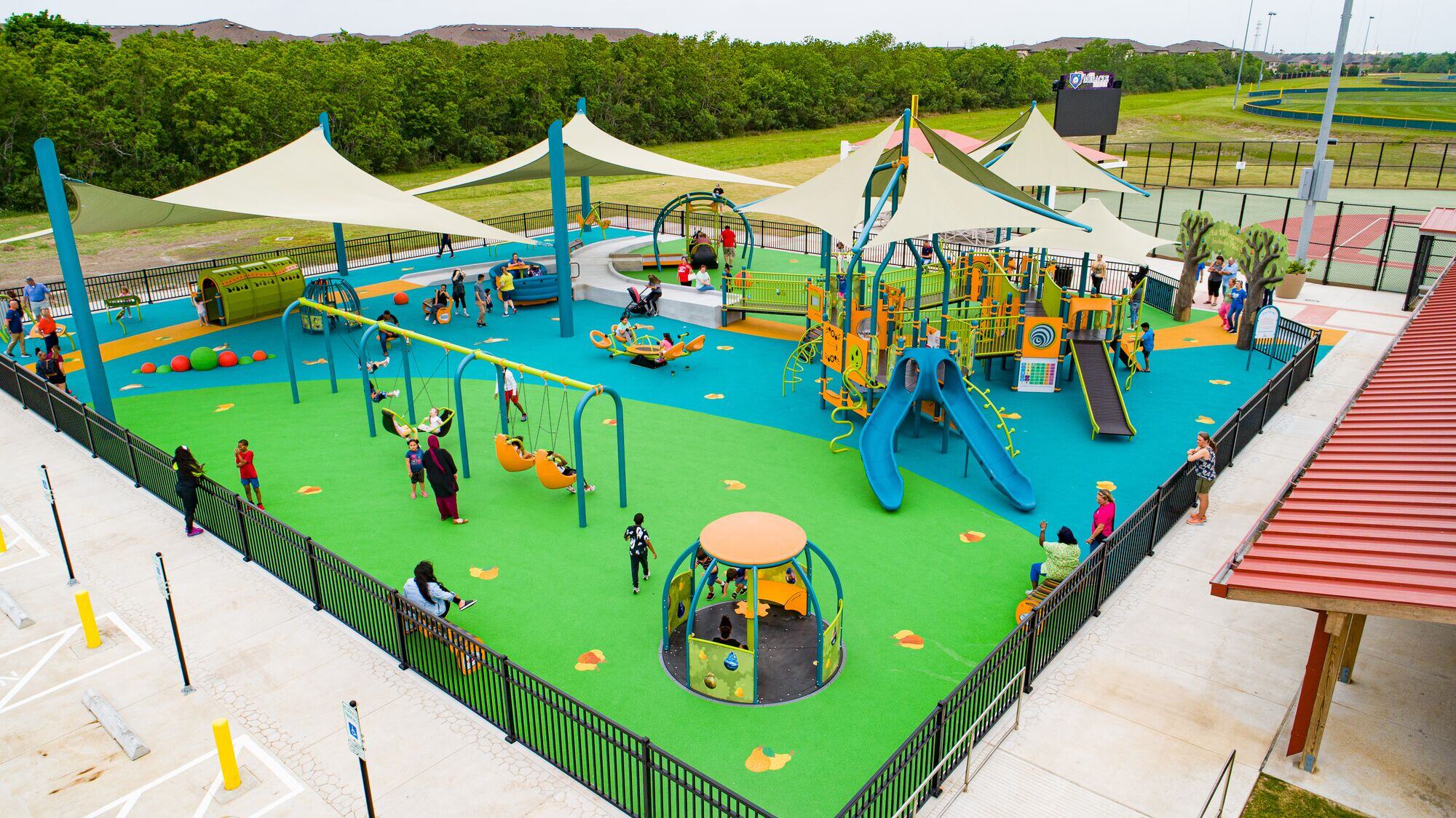 A vibrant and inclusive playground featuring shade structures, poured-in-play safety surfacing, and various accessible play elements, exemplifying the concept of all access playgrounds.