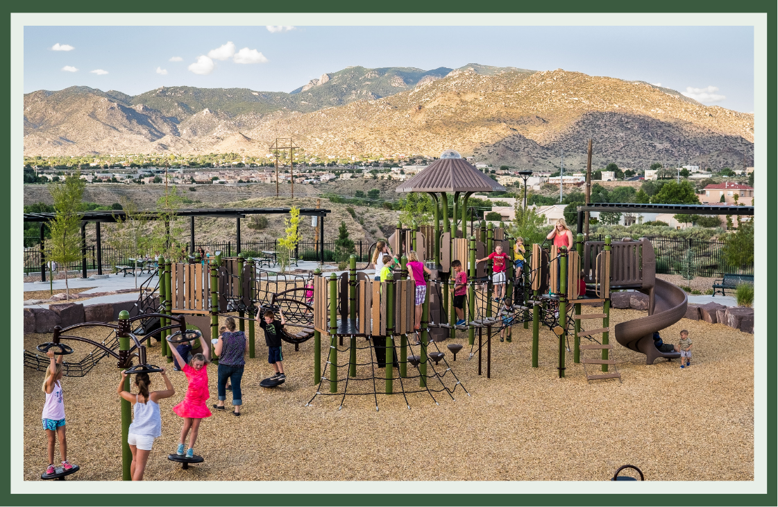 Earth-toned playground with a gazebo-topped tower, climbing nets and a curving slide, set against desert mountains so the design mirrors its landscape.
