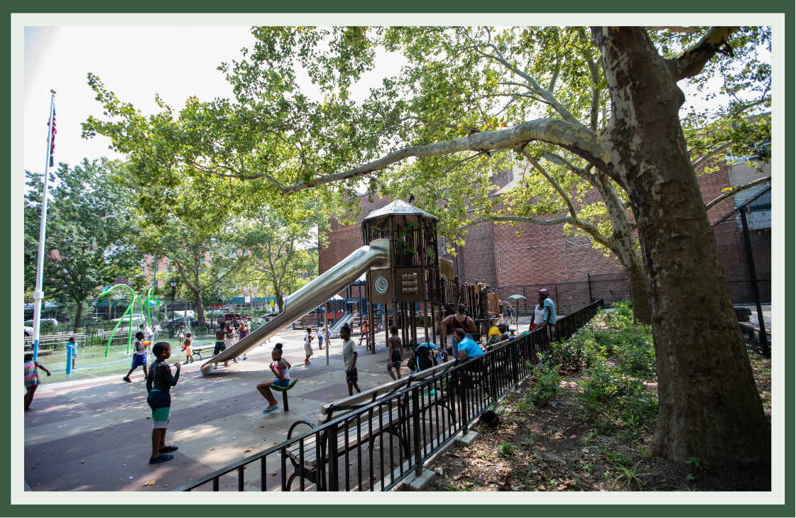Children playing on a treehouse-style tower with a slide under the canopy of a large shade tree in an urban neighborhood park.